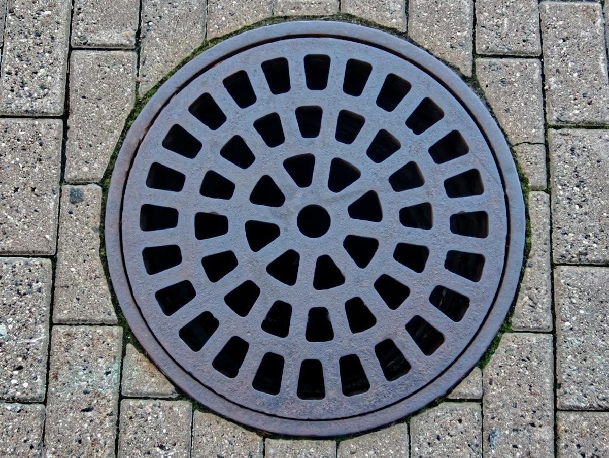 Industrie et prestations liées : taque d’égout en fonte sur un trottoir pavé